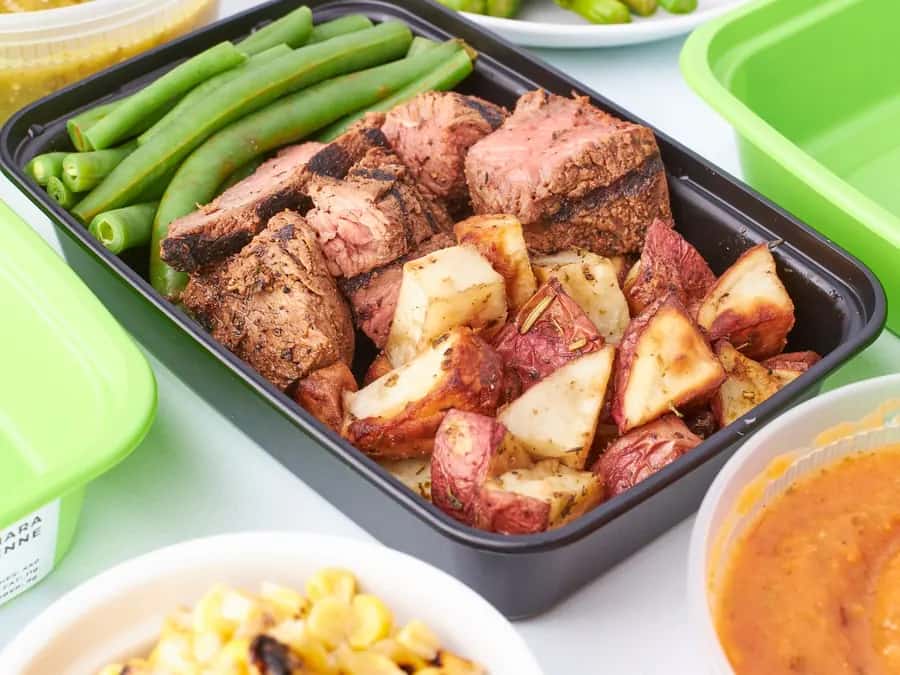 A prepared meal of sliced steak, green beans and roast potatoes in a container.