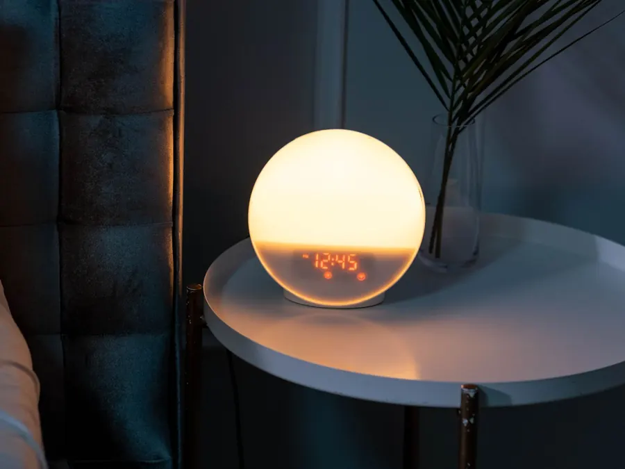 A glowing round bedside lamp showing 12:45, on a side table in a dim room.
