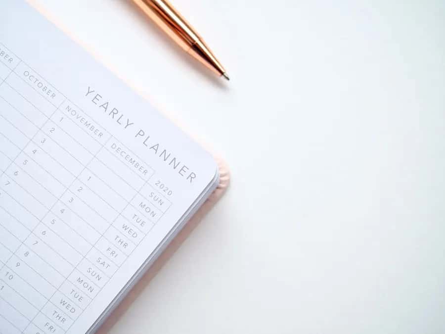 An open yearly planner beside a gold pen on a white surface.
