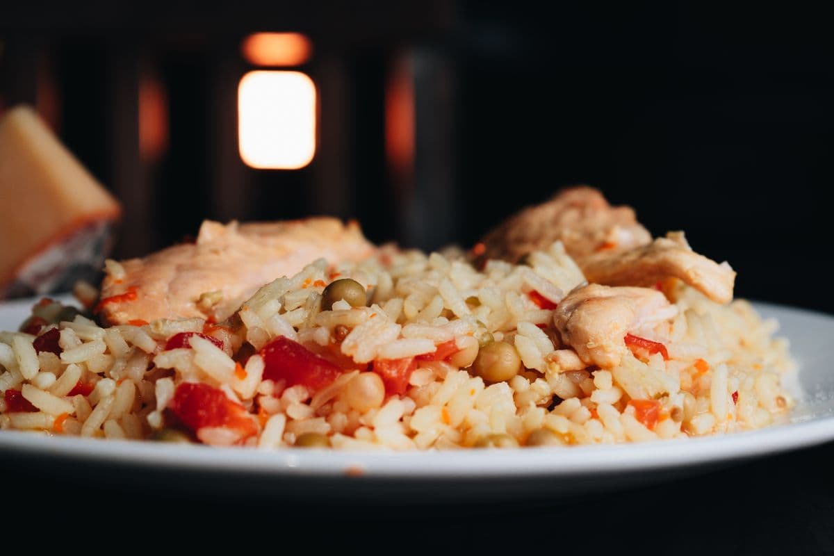 A plate of rice with chicken, peas, and tomato — a protein, grain, and vegetable meal.