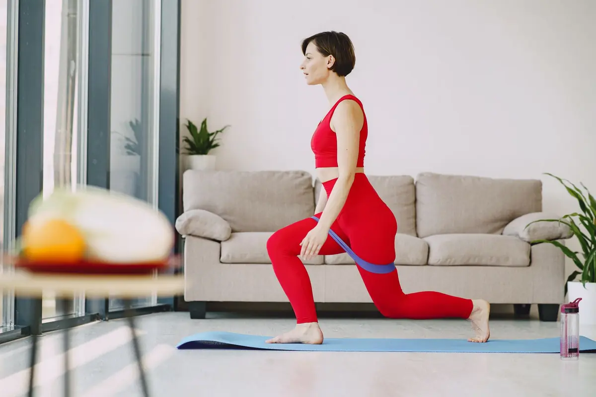 A person stretching into a lunge with a resistance band on a mat beside a sofa.