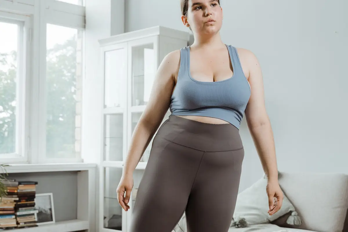 A person standing in a living room in a sports bra and leggings, arms at their sides.