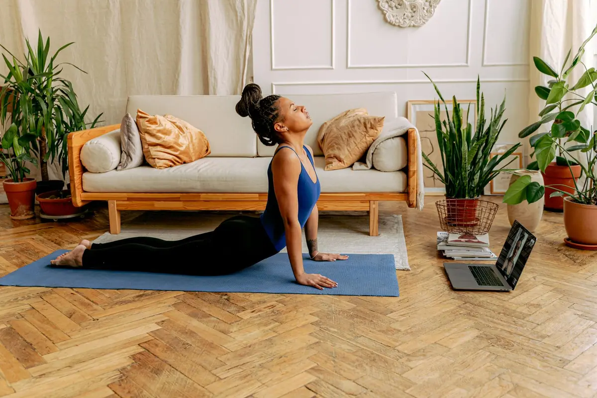 A person on a mat at home following a workout on a laptop set up beside them.